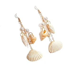 Detalle de pendientes estilo playa con conchas naturales y perlas blancas en cadenas oro.