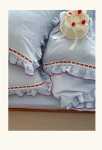 Detalle ropa cama gasa algodón, tela rayas azules con encaje lazo rojo y volante delicado.