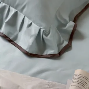 Cotton bedding detail showing light green ruffled pillowcase with elegant dark brown piping.