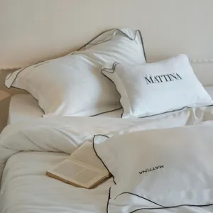 Luxury white Tencel bedding detail, elegant black piping, soft embroidered pillowcase design.