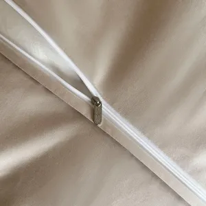 Detailed view of premium beige bedding fabric with smooth white zipper and logo pull.