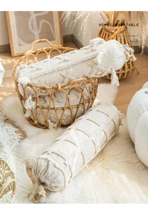 Boho cylindrical decorative pillow with tufted tassels and cozy rattan basket in living room.
