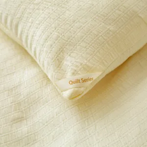 Close-up van zachte gele gewatteerde beddengoedstof met getextureerd ruitpatroon en label.