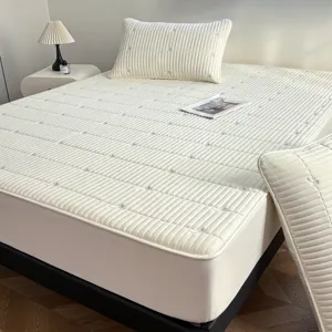 White quilted mattress protector with elegant embroidery, fitted sheet style for home.