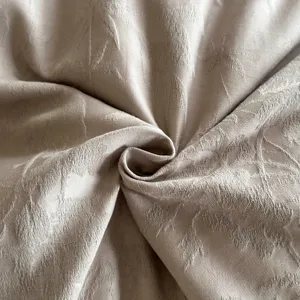 Close-up of beige jacquard cotton fabric showcasing fine botanical embossed texture details.