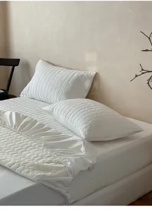 Protector de colchón acolchado blanco sábana bajera de algodón y funda de almohada detalle.