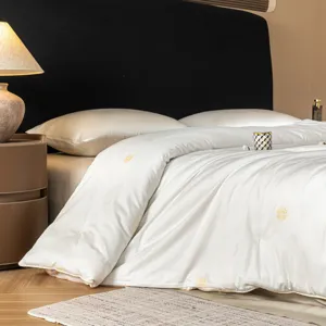 Detail view of luxurious white silk quilt with traditional golden embroidery for bedroom decor.