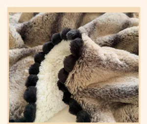 Detail view of luxurious faux rabbit fur ripple blanket with elegant black pom-pom fringe.