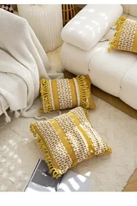 Housse de coussin décorative jaune style bohème avec franges blanches et motif touffeté.