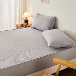 Coprimaterasso impermeabile trapuntato grigio con due cuscini in camera da letto accogliente.