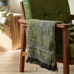Close-up view of a vintage green cotton jacquard throw blanket draped over a wooden chair arm.