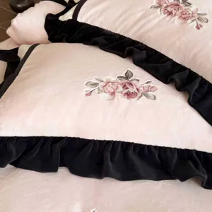 Nahaufnahme eines rosa Korallenfleece-Kopfkissenbezugs mit schwarzen Rüschen und Rosenstickerei.