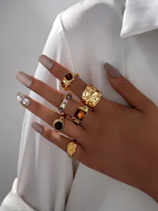 Close-up of multiple textured gold rings with amber and colorful stone accents.