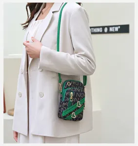 Detail view of the vertical crossbody phone bag with green strap and heart metal charms.