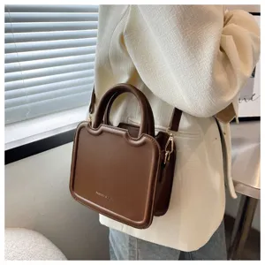 Close-up of the stylish brown leather handbag with unique frame design worn by a model.