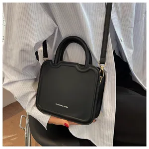 Detailed view of stylish black top-handle crossbody bag with modern curved design and hardware.