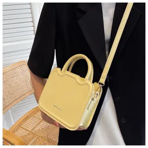Detailed view of trendy yellow leather handbag with unique wavy top design and shoulder strap.
