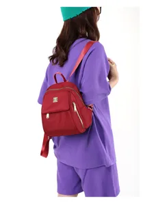 Detail view of a stylish red nylon mini backpack worn by a model, showing side pocket.