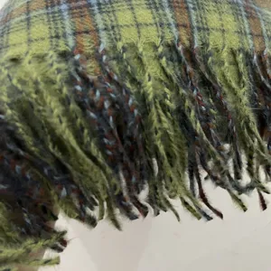 Green plaid scarf detail shot showing delicate tassel fringe texture and cozy winter fabric.