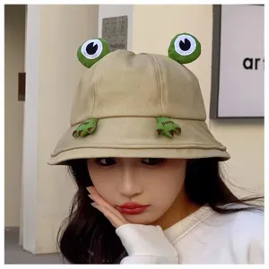 Cute cartoon frog bucket hat detail closeup, khaki canvas fabric with 3D eyes and paws design.