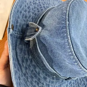 Close-up detail of vintage washed denim bucket hat, showing fine stitching and metal rivet hardware.