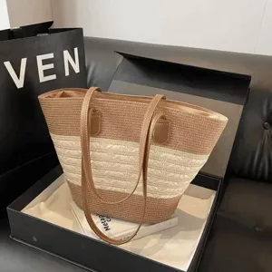 Detailed view of the woven straw tote bag with brown and beige color block design and leather handles.