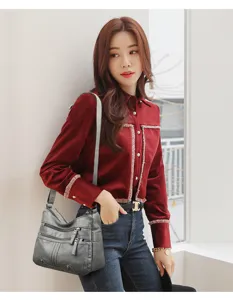 Detail view of a multi-pocket soft leather shoulder bag worn by a model indoors.