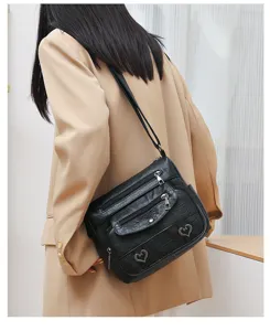 Detailed view of women's black soft leather shoulder bag with multiple zippered pockets and hearts.