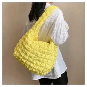 Detail shot of stylish yellow quilted cloud shoulder bag worn by model, soft neutral background.