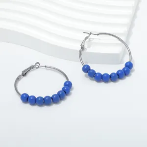 Close-up view of blue beaded hoop earrings featuring sleek metal loops on a white textured background