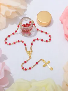 Vista dettagliata di una collana rosario con perline rosse, croce dorata e bottiglia di vetro.