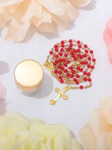Primo piano dettagliato di una collana rosario con perle rosse da 4mm e croce dorata.