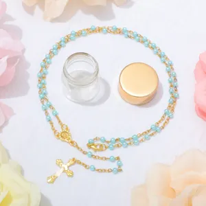 Collana rosario perle blu con ciondolo croce e bottiglia di vetro, elegante gioiello religioso.