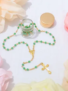 Dettaglio ravvicinato della collana con croce rosario battesimo perle verdi con bottiglia.