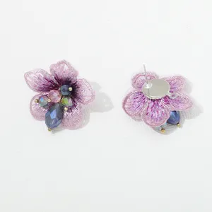 Detailweergave van paarse stoffen bloem oorknopjes met kristallen kralen en metalen steker.