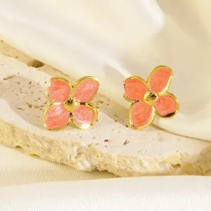 Primo piano dettagliato di orecchini a fiore smaltato rosa con bordo dorato su pietra.