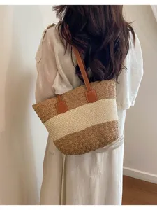 Gros plan sur un sac à épaule élégant en paille tressée avec un design bicolore et des anses.