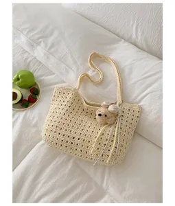 Gros plan détail du sac porté épaule crocheté beige ajouré avec joli pendentif ours en peluche.