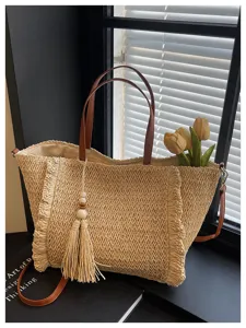 Detail shot of stylish straw woven tote bag with brown leather handles, tassel and floral decor.