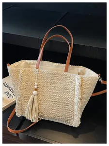 Casual woven straw tote bag with brown leather handles, fringe decor, and chic tassel charm.