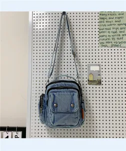Close-up view of casual denim crossbody bag with multiple zipper pockets and adjustable strap.