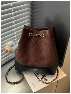 Detailed view of brown suede and black leather quilted bucket bag with chain strap charm.