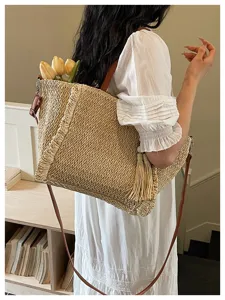 Detailed shot of a stylish straw woven shoulder bag with fringe and brown straps for summer beach.