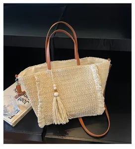 Woven straw tote bag detail, featuring brown handles, stylish fringe trim, and a tassel pendant.