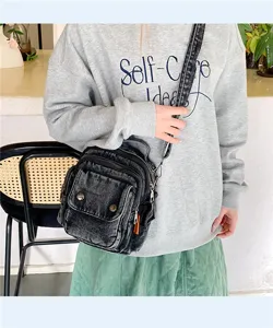 Close-up detail of black denim crossbody bag featuring multiple zippers and pockets.