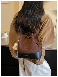 Detail view of the brown suede quilted bucket bag with chain strap worn on back, autumn style.