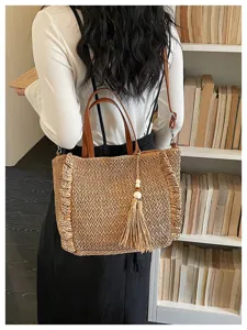Casual straw woven shoulder bag with brown leather handles and chic tassel charm for women.