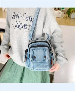 Detailed view of casual denim cross-body bag featuring double zippers and front pocket.