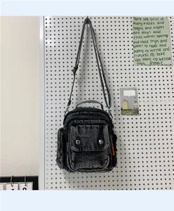 Detail shot of black washed denim crossbody bag hanging on pegboard with adjustable strap.