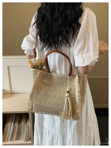 Woven straw shoulder bag for women, stylish vacation tote with leather handles and chic tassel.